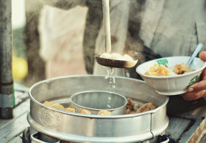 A street vendor ladles hot bakso into a bowl
